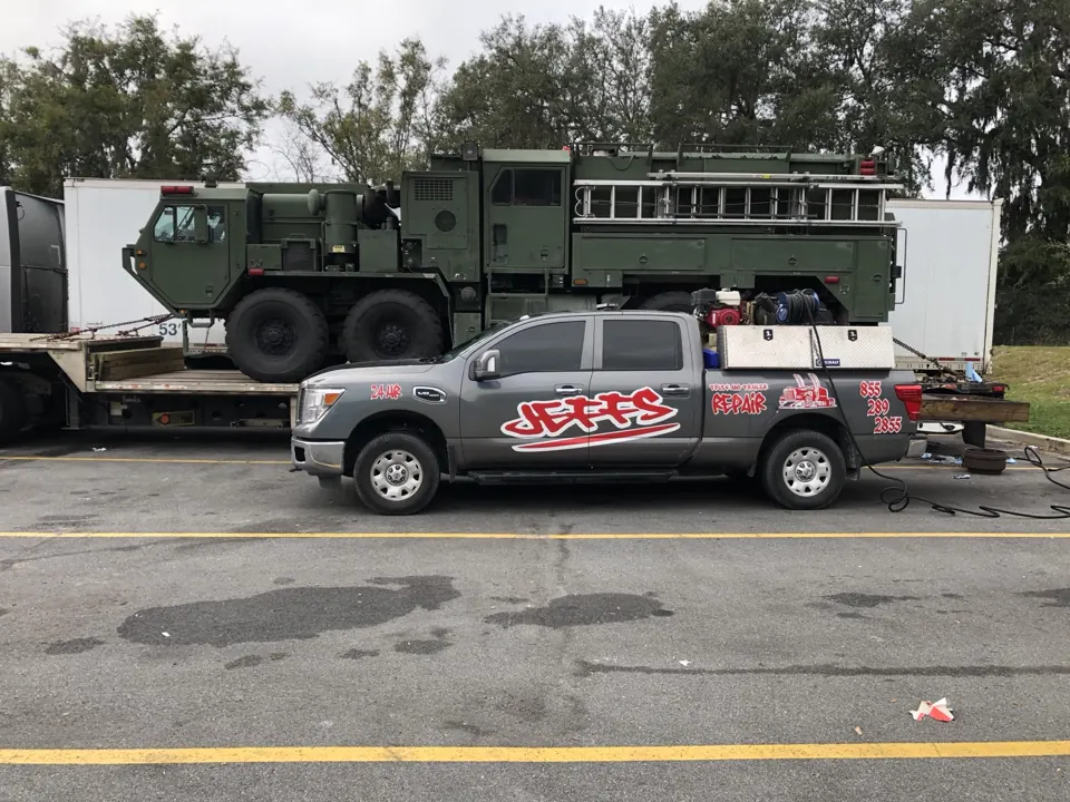 Branded JTR service truck beside a heavy off-road vehicle on a lowboy trailer